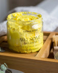 Citrus River Yellow Salt Body Scrub in bathroom on bath rack with towel, leaves & nail brush