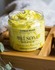 Citrus River Yellow Whipped Soap on bath rack in bathroom with leaves, towel & nail brush