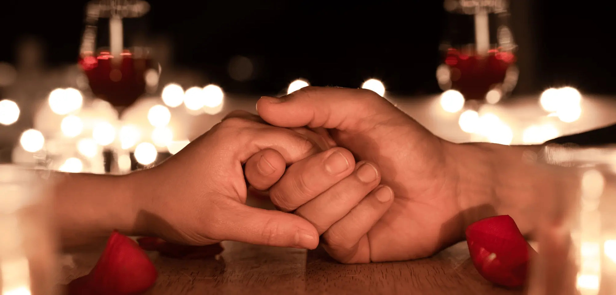 2 people holding hands with wine and lights 