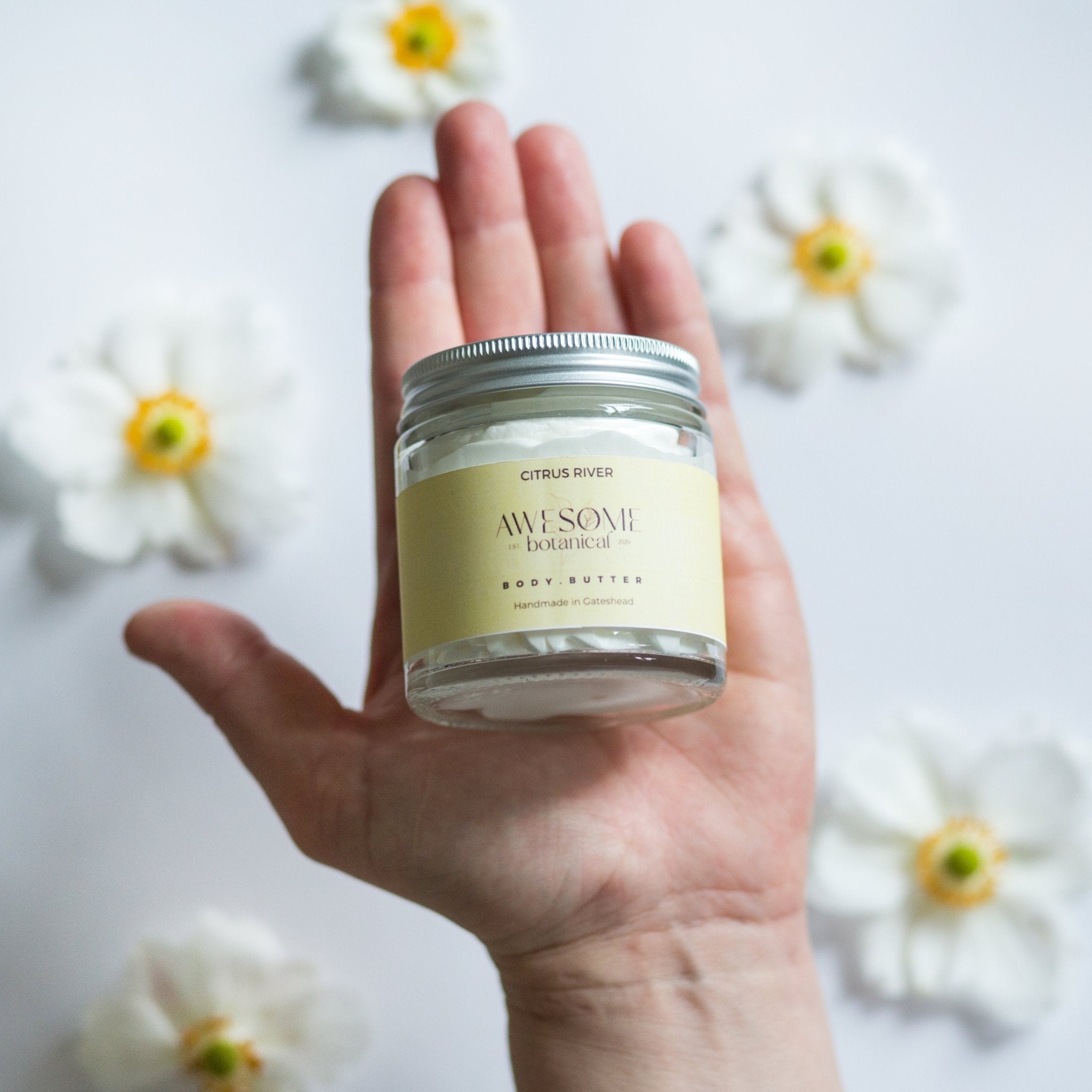 Energise Body Butter in hand with white flower background