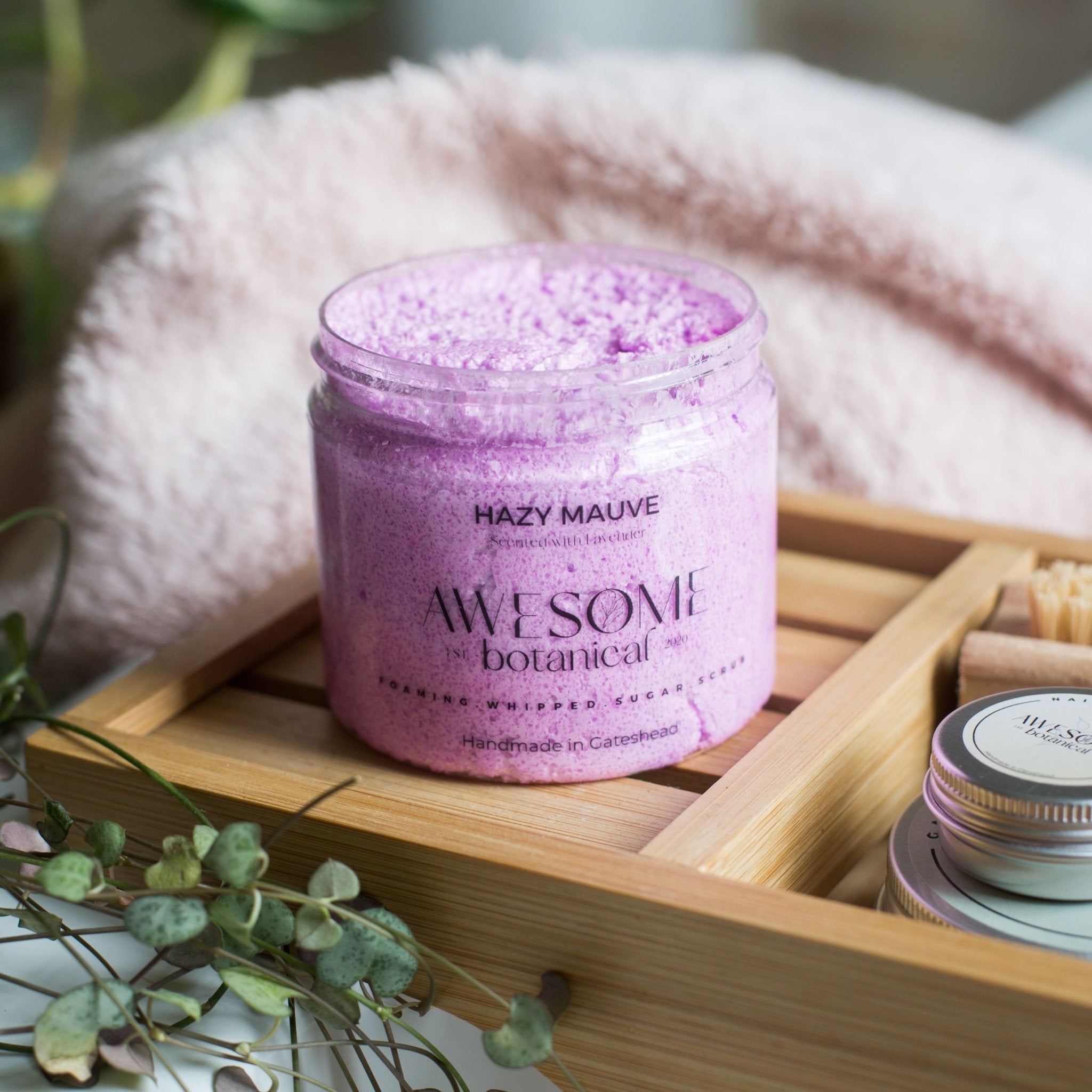 Hazy Mauve Lavender sugar scrub on bath rack with towel and plant in background